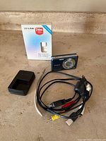 Sony Cybershot 12.1 MP camera with charger, cables, and TP-Link USB adapter box arranged on a beige surface