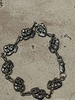 Photo of vintage sterling silver bracelet with linked laugh and cry theatrical masks on concrete surface.
