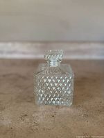 Front view of vintage square-shaped clear glass decanter with diamond cut pattern and glass stopper.