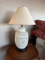 Full view of the vintage Blanc De Chine style lamp showing its reticulated porcelain body on wooden base and cream fabric shade on top.
