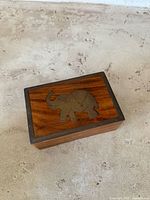 Front angled view of the small wooden trinket box with brass elephant inlay on lid, showing wood grain and detailed brass design.