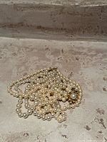 Photo shows a tangled group of cream-colored costume pearls, including necklace and bracelet, resting on a textured surface.