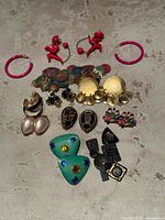 Top-down photo showing entire lot of vintage earrings arranged on a neutral surface.