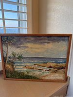 Framed coastal painting with waves, rocks, greenery, cloudy sky, and signature "Timmermans" in lower right corner.