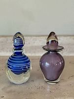 Two vintage Murano glass perfume bottles side by side on a surface, clear background.