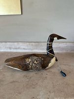 Full side view of the wooden duck decoy highlighting the natural wood grain, bark on the back, and attached weight.