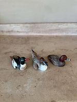 Three vintage Heritage Decoy miniature duck figures displayed side by side on a flat surface.