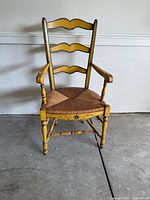 Front view of vintage ladder back dining chair with yellow painted wood and wicker seat showing armrests and turned legs.