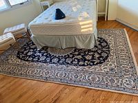 Full view of rectangular rug under bed showing navy center and ivory floral border