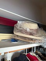 White woven straw hat in plastic on top of stacked straw and felt hats