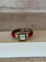 Front view of vintage women's wristwatch showing red band and square gold-tone case with white dial.