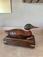 Full view of wooden Mallard duck decoy on wooden box base with brass shell.