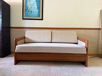 Front view of the teak framed sofa bed with cushions in beige upholstery.