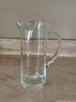 Clear pressed glass cocktail pitcher shown from front on marble surface with neutral background.
