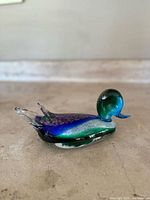 Side view of the Murano glass duck figurine showing blue and green body with gold flecks and clear tail.