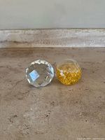 Two vintage Swarovski paperweights on stone surface, one clear faceted crystal and one transparent with gold flakes.
