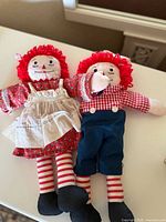 Front view of Raggedy Ann and Raggedy Andy dolls lying side by side showing detailed clothing and face.