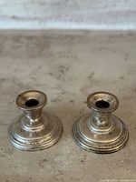 Two short vintage sterling silver candlesticks with visible patina on a neutral surface.