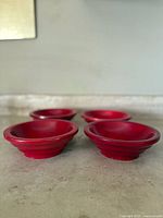 Front view of 4 red handmade bowls showing their shallow shape and flared rims on a marble surface.