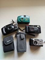 Top-down photo showing five vintage cameras and two camera cases on a flat surface.