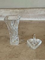 Photo showing entire clear crystal vase with flared octagonal top and heart-shaped ring holder with ring peg on a beige stone surface.
