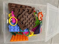 Clear plastic bin with various brown silicone chocolate and candy moulds on top and assorted colorful cookie cutters beneath