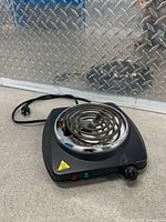 Front view showing black plastic base, round coil element, temperature knob and indicator lights.