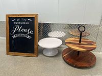 Wooden two-tier display stand, white plastic pedestal cake stand, and wooden Instagram chalkboard with text