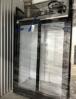Front view of shrink-wrapped commercial glass door cooler showing two glass doors and black frame