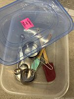 Gluten free baking supplies including measuring spoons, cups, spatula, utensil brush, wooden handled utensils inside a clear plastic tote container with lid