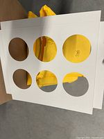 White cardboard cupcake box insert with six circular holes, placed over a yellow background.