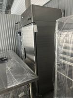 Full view of the stainless steel upright freezer in storage unit alongside a wrapped stainless steel table.