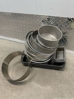 Stack of various round metal baking pans with a few small rectangular pans placed on a black tray.