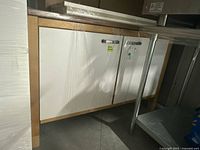 Full view of IKEA Värde storage cabinet wrapped in plastic showing birch wood frame and white panels with blue tape on cabinet doors.