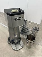 Front view of mixer with whisk attached and stainless steel cup at base