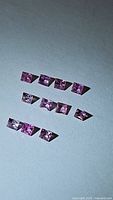 Lot of 10 princess cut pink sapphires arranged on a plain surface, clearly showing size and clarity.