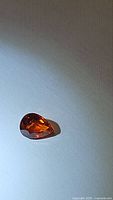 Photo of pear-shaped natural spessartite garnet gemstone with orange hue on white background.