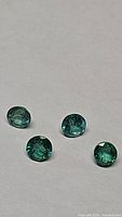 Four natural round cut emerald gemstones shown on a white background, highlighting their color and clarity.