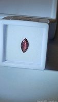 Marquise cut sapphire displayed in white jewelry case, shows elongated shape and deep raspberry color.