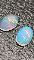 Two oval cabochon untreated natural Ethiopian opals on textured black background, showing vivid rainbow colors and translucency.