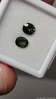 Two oval faceted stones in display case, greenish hue visible