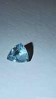 Close-up photo of a light blue trillion cut aquamarine gemstone on a white background showing facets and clarity.