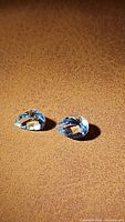 Two pear cut light blue aquamarine gemstones on a brown textured surface, faceted and transparent showing clarity and color.