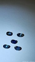 Five oval cut natural blue sapphires under direct light showing varying blue hues and faceting.