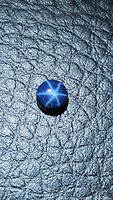 Top view of round cabochon blue star sapphire showing six-ray asterism and surface texture on black textured background.
