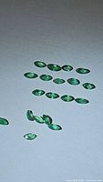 Lot of natural marquis cut emeralds arranged on a flat surface showing size and shape.