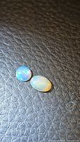 Two natural Ethiopian opal stones on textured black surface showing multicolored play of color predominantly blue and green hues.