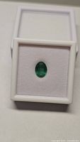 Oval green emerald in white display box, top-down view