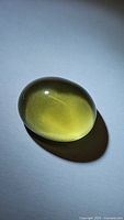 Oval cabochon lemon citrine gemstone shown with smooth polished surface and light reflection on plain background.