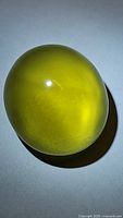 Large oval lemon citrine gemstone shown on white background under light. Visible deep lemon yellow-green color and polished domed surface.